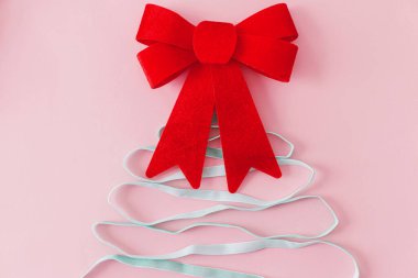 Kırmızı fiyonklu modern Noel ağacı. Kış tatili konsepti. Pembe arka planda büyük kırmızı fiyonk ve ağaç şeklinde yeşil kurdele. Yaratıcı kompozisyon. İyi tatiller.!