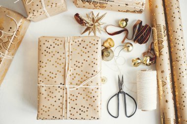 Stylish christmas gift flat lay. Modern wrapped christmas gift boxes, festive paper, golden ornaments and thread composition on white wooden background. Merry Christmas!