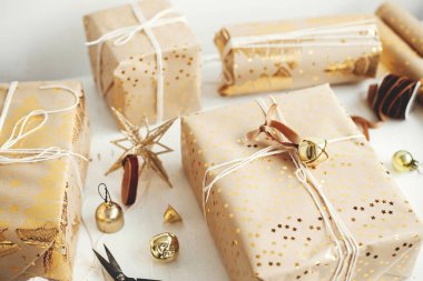 Altın Noel hediyeleri çok şık. Huysuz afiş. Modern ambalajlı Noel hediye kutuları, bayram kağıdı, altın süsler ve beyaz ahşap arka planda iplik kompozisyonu. Mutlu Noeller.!