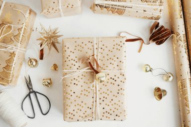 Mutlu Noeller! Şık altın noel hediyeleri düzdü. Modern ambalajlı Noel hediye kutuları, bayram kağıdı, altın süsler ve beyaz ahşap arka planda iplik kompozisyonu. Huysuz bayrak
