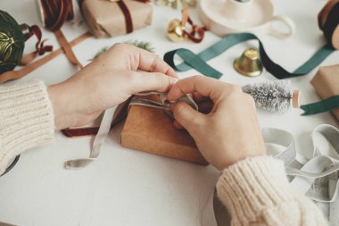 Eller şık bir Noel hediyesi paketliyor. Noel hediyesini kadife kurdele ve beyaz ahşap süslemelerle hazırlayan kişi. Mutlu Noeller! Estetik kış tatili