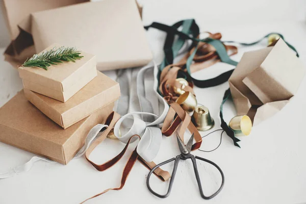Merry Christmas! Sustainable holidays, wrapping stylish eco christmas gifts composition. Simple craft gift boxes, velvet ribbons, christmas bells, fir branch and scissors on white background.