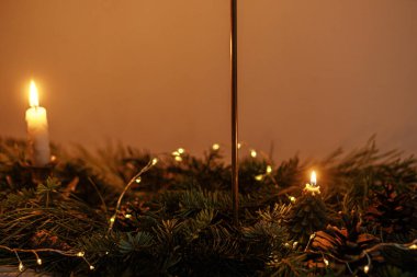 Akşam vakti karanlık odada köknar dalları ve altın ışıklarla süslü bir Noel mumu. Atmosferik Noel ya da yeni yıl arifesi. Altın ışıklı ve çam desenli karamsar gece görüntüsü