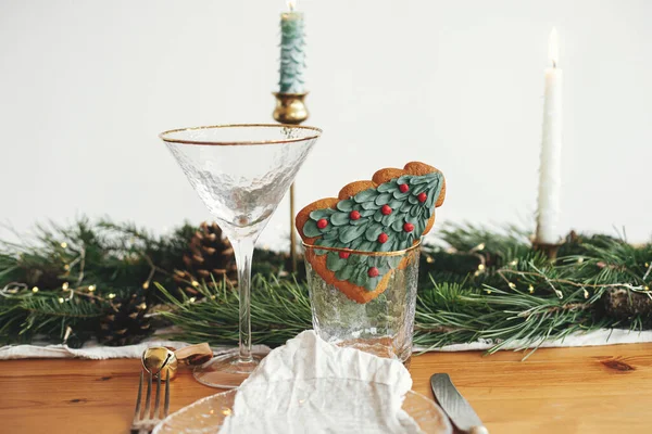 圣诞餐桌摆设 圣诞树饼干在玻璃中 盘与亚麻布餐巾 老式餐具 冷杉树枝与金光和松果在桌子上 创意假期安排 — 图库照片