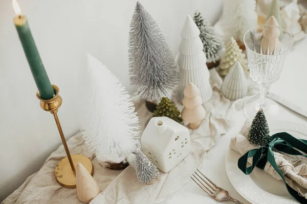 スタイリッシュなクリスマステーブルの設定 プレート上のリボンと鐘 ヴィンテージカトラリー ワイングラス モダンなクリスマスツリーと白素朴なテーブルの上の家でお祝いのナプキン 休日ブランチ — ストック写真