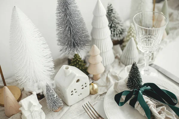 スタイリッシュなクリスマステーブルの設定 プレート上のリボンと鐘 ヴィンテージカトラリー ワイングラス モダンなクリスマスツリーと白素朴なテーブルの上の家でお祝いのナプキン 休日ブランチ — ストック写真