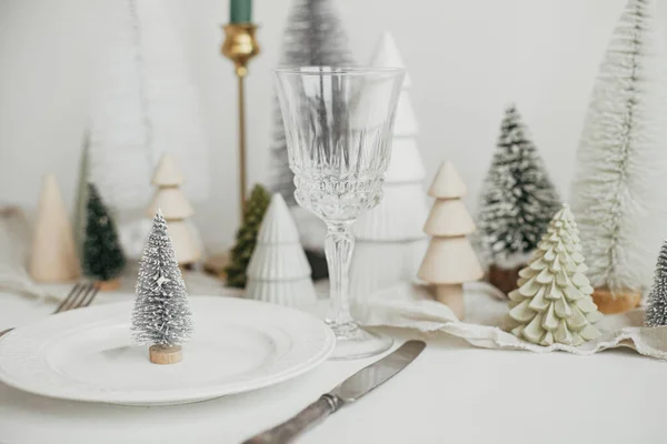 スタイリッシュなクリスマステーブルの設定 プレート上の近代的な小さなクリスマスツリー ヴィンテージのカトラリー ワイングラス モダンなクリスマスツリーや白素朴なテーブルの上の家 休日のブランチ 新年のお祝い — ストック写真