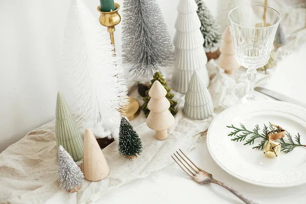现代圣诞餐桌设置 雪松枝条 盘中有铃铛 老式餐具 喜庆的小圣诞树 白色乡村餐桌上的房子 餐桌的假日安排 — 图库照片