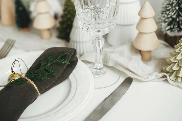 クリスマステーブルのセッティング プレート上の鐘やモミとスタイリッシュなナプキン ヴィンテージカトラリー 白い素朴なテーブルの上にお祝いの小さなクリスマスツリー テーブルの休日の配置 — ストック写真