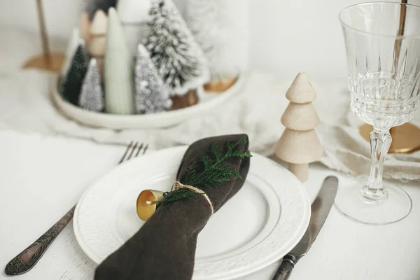 クリスマステーブルのセッティング プレート上の鐘やモミとスタイリッシュなナプキン ヴィンテージカトラリー 白い素朴なテーブルの上にお祝いの小さなクリスマスツリー テーブルの休日の配置 — ストック写真