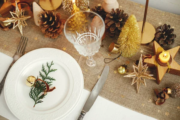 クリスマスの豪華なテーブルの設定 板の上に鐘を持つ杉の枝 ヴィンテージカトラリー 黄金の小さなクリスマスツリーやテーブルの上の装飾品 テーブルの休日の配置 — ストック写真