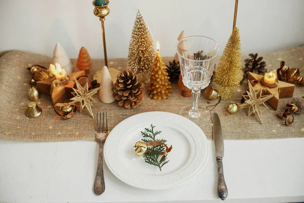 スタイリッシュなクリスマステーブルの設定 プレート上の鐘 ヴィンテージカトラリー ワイングラス モダンな黄金のクリスマスツリーや素朴なテーブルの上のキャンドルとフェアブランチ 休日のブランチ 新年のお祝い — ストック写真