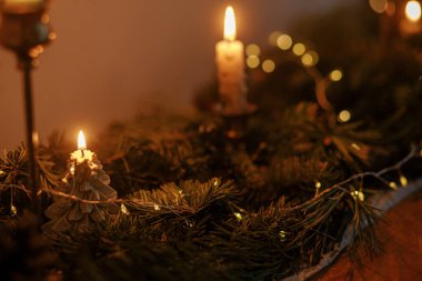 Akşam vakti karanlık odada köknar dalları ve altın ışıklarla süslü bir Noel mumu. Atmosferik Noel ya da yeni yıl arifesi. Altın ışıklı ve çam desenli karamsar gece görüntüsü