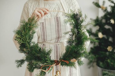 Şık, modern bir Noel çelengi taşıyan kadife kurdeleli ve şenlik odasında altın çan çalan bir kadın. Tatil dekoru, karamsar bir görüntü. Mutlu Noeller ve mutlu tatiller!