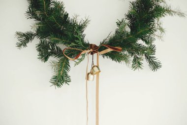 Beyaz arka planda kadife kurdeleli ve altın zilli modern Noel çelengi. Mutlu Noeller ve mutlu tatiller! Kış tatili dekorasyonu, karamsar bir görüntü. Boho çelengi
