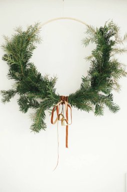 Mutlu Noeller ve mutlu tatiller! Beyaz arka planda kadife kurdeleli ve altın zilli modern Noel çelengi. Kış tatili dekorasyonu, karamsar bir görüntü. Boho çelengi