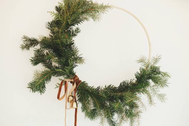 Kadife kurdeleli modern Noel çelengi ve beyaz duvarda asılı altın çanlar yakın plan. Mutlu Noeller ve mutlu tatiller! Kış tatili dekorasyonu, karamsar bir görüntü. Boho çelengi