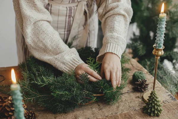 让圣诞乡村花环 女人的手拿着枞树枝头 金色铃铛 蜡烛在乡村木桌上做花圈 喜怒无常的假日形象 寒假工作坊 — 图库照片