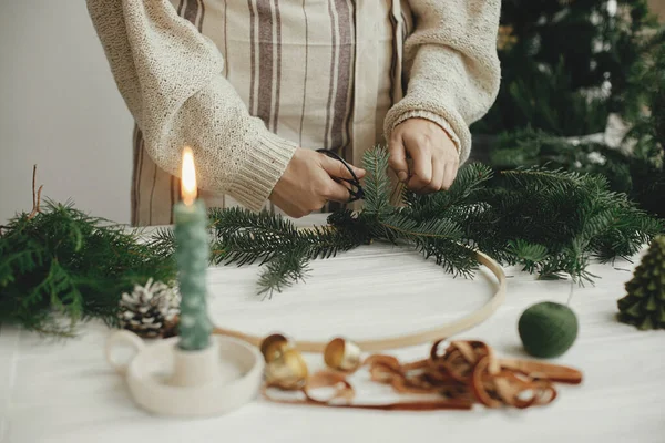 女人的手拿着冷杉树枝 用剪刀 松果在白色木制桌子上做着现代圣诞花环 假日作坊 做Boho花环 冬季装饰 喜怒无常的形象 — 图库照片