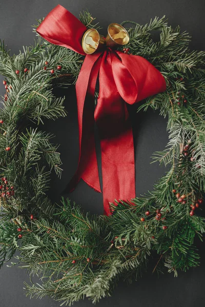 現代のクリスマスリースフラットレイアウト 暗い背景に赤いリボンと黄金の鐘とスタイリッシュなクリスマスの花輪 冬の休日の装飾 メリークリスマスとハッピーホリデー — ストック写真