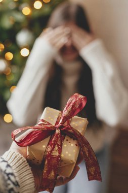 Mutlu Noeller ve mutlu tatiller! Mutlu bir kadının gözlerini kapayıp sürpriz beklediği arkaplanda Noel hediyesi kutusu. Atmosferik odadaki Noel ağacında hediyelerimizi değiş tokuş ediyoruz.