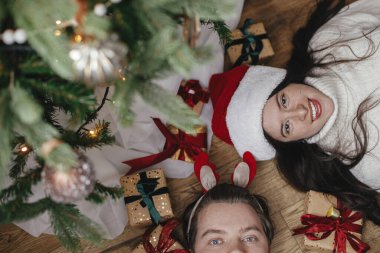 Noel ağacının altında Noel hediyeleriyle uzanan mutlu, genç bir aile. Dekoratif bir odada, üst tarafta. Mutlu Noeller ve mutlu tatiller! Çift hediyelerle eğleniyor.