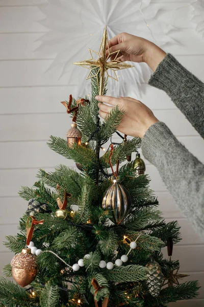 在大气节日的房间里 用手装饰着有时尚色彩的圣诞树 圣诞快乐 准备寒假 穿着舒适毛衣的女人把老明星放在树梢上 — 图库照片
