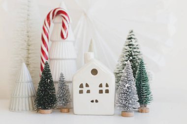 Mutlu Noeller ve mutlu tatiller! Beyaz masa üzerinde şık küçük Noel ağaçları, evler ve baston şekerler. Modern Noel sahnesi, minyatür karlı köy. Kış bayrağı, İskandinav dekoru