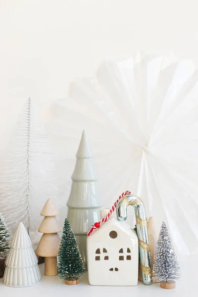 白いテーブルの上にスタイリッシュな小さなクリスマスツリー 家やお菓子の杖 メリークリスマスとハッピーホリデー 現代のお祝いのシーン ミニチュア雪の村 冬のバナー スカンディナヴィアの装飾 — ストック写真
