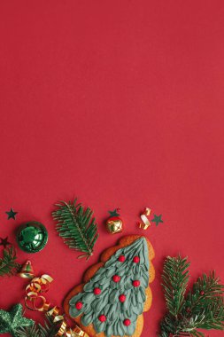 Modern noel yatağı. Şık Noel ağacı kurabiyeleri, takılar, köknar dalları, kırmızı arka planda konfeti. Mevsimlik tebrik kartı, mesaj için yer. Mutlu Noeller! Kış tatili
