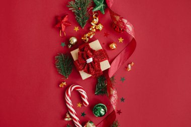 Modern noel yatağı. Şık bir Noel hediyesi, takılar, köknar dalları, baston şekerler, kırmızı arka planda konfeti. Mevsimlik tebrik kartı, mesaj için yer. Mutlu Noeller! Kış tatili afişi