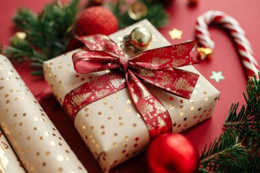Mutlu Noeller ve mutlu tatiller! Modern Noel kompozisyonu. Şık bir Noel hediyesi, ambalaj kağıdı, köknar dalları, baston şekerler ve kırmızı arka planda mücevherler. Bayram bayrağı