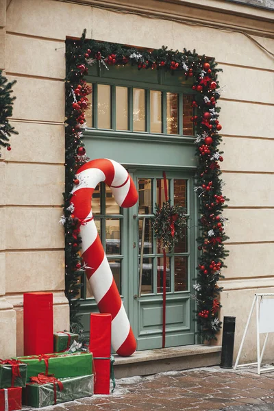 スタイリッシュな大きなキャンディー杖 赤と緑のラップクリスマスプレゼント モミの枝 建物の外観上の花輪 街の通りで近代的なクリスマスの装飾 ヨーロッパでの冬の休暇 — ストック写真