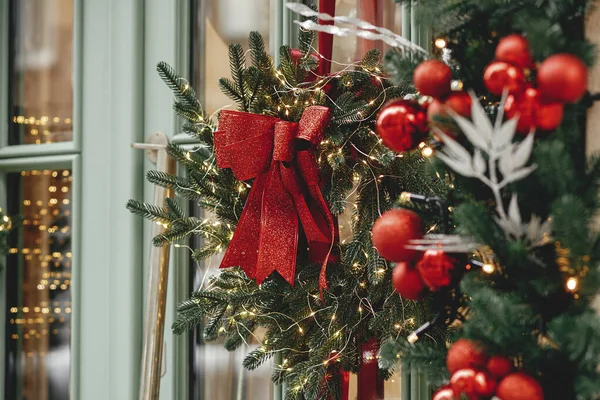 别致的圣诞花环 红色的蝴蝶结和冷杉枝条 外层有灌木丛和灯光 现代圣诞节装饰在城市街道上 欧洲寒假 圣诞快乐 — 图库照片
