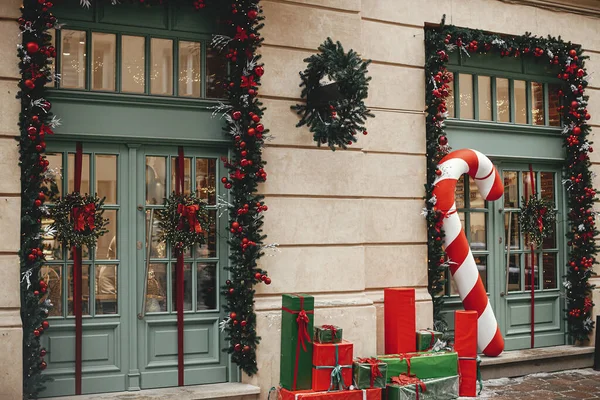 スタイリッシュな大きなキャンディー杖 赤と緑のラップクリスマスプレゼント モミの枝 建物の外観上の花輪 街の通りで近代的なクリスマスの装飾 ヨーロッパでの冬の休暇 — ストック写真