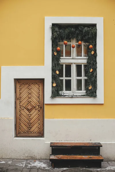 Sarı Binanın Beyaz Penceresinde Portakallı Mandallı Noel Dalları Şehir Sokaklarında — Stok fotoğraf