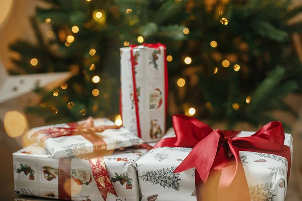 メリークリスマスとハッピーホリデー 黄金のライトボケとクリスマスツリーでスタイリッシュなクリスマスプレゼント 部屋の装飾された木の下に赤いリボンで包まれたクリスマスプレゼント 大気旗 — ストック写真