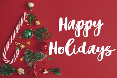 Noel ağacı, kış tatili konsepti. Kırmızı arka planda köknar dalları, mücevherler, altın konfeti ve şeker kamışından yapılmış şık bir Noel ağacı, düz bir zemin. Yaratıcı bir fikir. Modern bayrak