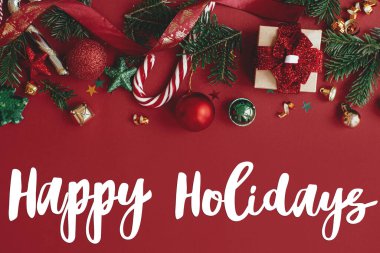 Noel hediyesi, mücevher, köknar dalı, konfeti ve şeker kamışını kırmızı arka planda düzleştiren mutlu bayramlar tabelası. Sezonun tebrik kartı. Noel kartpostalı