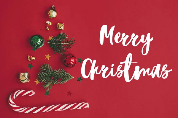 モミの枝 赤ちゃん 金のコンフェッティと赤い背景フラットレイアウト上のキャンディー杖で作られたクリスマスツリー上のメリークリスマステキスト シーズンのグリーティングカード 手書きのサイン — ストック写真