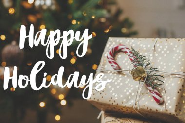 Noel ağacında altın ışıklarla süslenmiş şık Noel hediyelerine Mutlu Tatiller tabelası. Sezonun tebrik kartı. Noel kartpostalı