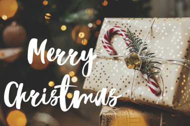 Altın ışıklı Noel ağacındaki Noel hediyeleriyle ilgili mutlu noel mesajları Bokeh. Sezonun tebrik kartı. El yazısıyla yazılmış işaret. Şenlikli kartpostal