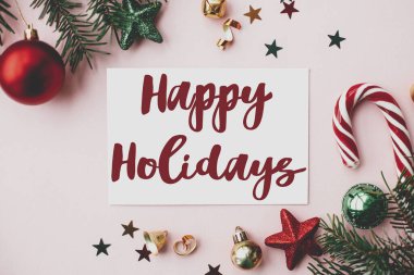 Kırmızı Noel süslemeleri, köknar dalları ve süslemeleri pembe arka planda olan kartla mutlu tatiller tabelası. Sezonun tebrik kartı. Noel kartpostalı