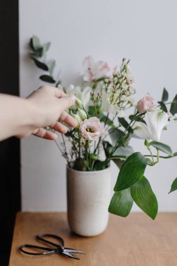 Çiçekçi, ahşap arka planda makasıyla güzel, taze çiçekler düzenliyor. Çiçek dekoru. Ahşap pencere pervazında seramik vazoda el ve şık bir buket. Bahar modern buket