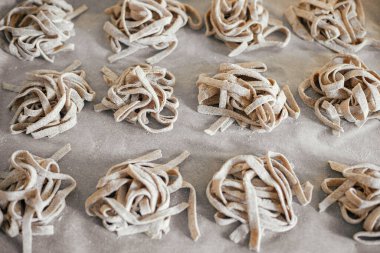 Homemade pasta. Dry fettuccine noodles in nests on baking tray close up. Making whole-grain pasta in kitchen, home made italian dinner