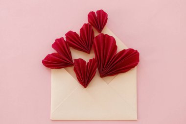 Stylish envelope with red hearts flat lay on pink paper background. Modern valentine card, space for text. Happy Valentine's day! Love banner. Creative letter composition