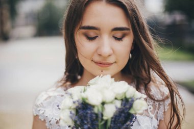 Şehvetli gelin portresi, gül buketi ve lavanta desenli şık bir elbise. Provence düğünü. Avrupa şehrinin güneşli caddesinde poz veren şık, eski moda elbiseli güzel gelin
