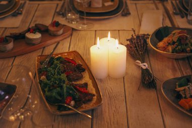 Stylish delicious table with food and drinks, burning candles and flowers at evening provence wedding reception in restaurant. Christmas feast or new year party. Luxury catering at banquets