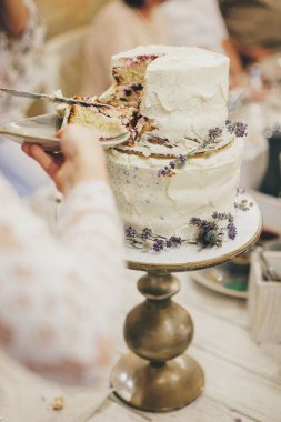 Gelin ve damadın elleri restoranda lezzetli modern pastalar kesiyor, yakın plan. Güzel bir çift ellerinde lezzetli bir düğün pastası tutuyor. Provence düğün resepsiyonu