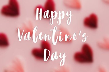 Bulanık pembe ve kırmızı kalpler üzerine mutlu sevgililer günü metinleri pembe kağıt zemin üzerinde yatıyordu. Yaratıcı modern Sevgililer Günü tebrik kartı. El yazısı işareti